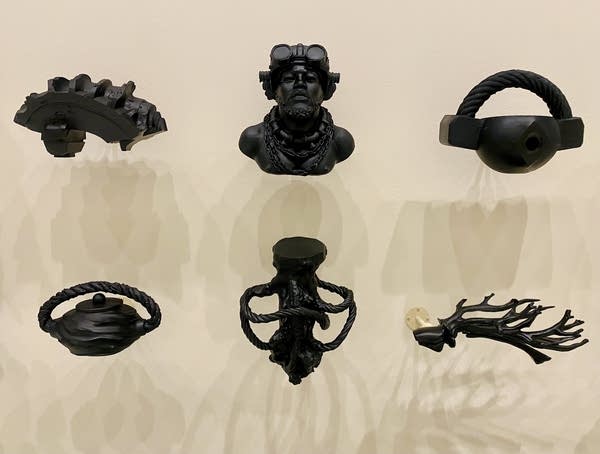 Black 3D-printed resin sculptures are hung from a white wall.