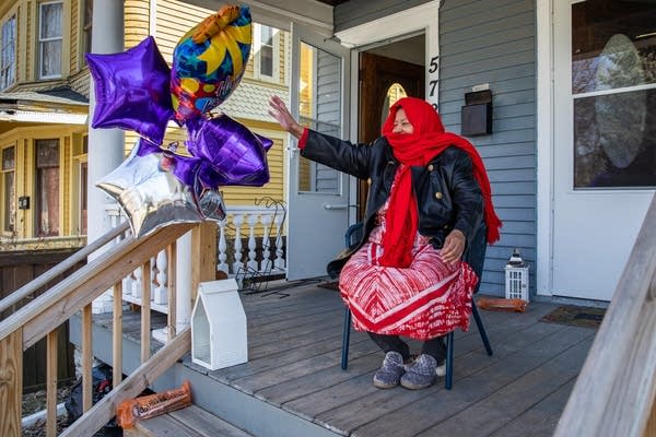 A woman in red waves from a porch with balloons.