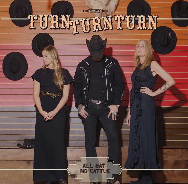 Three people stand for a photo in front of a display of cowboy hats