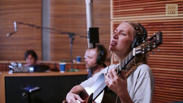 A musician sings and plays guitar in a recording studio