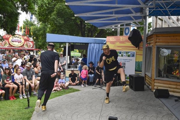 Two vocalists sing and dance on an outdoor stage