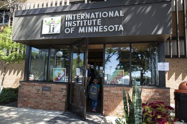 People walk into the front door of a brick and glass building.