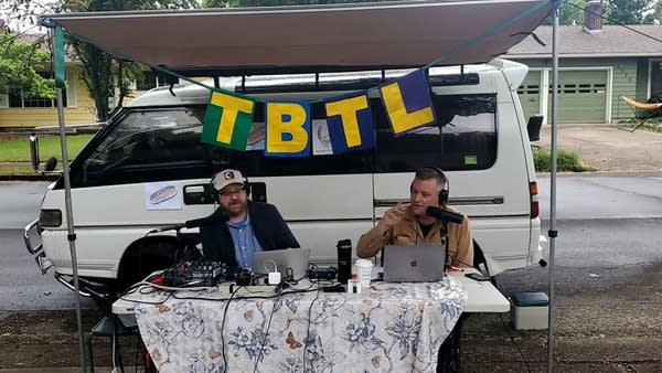Luke and Andrew podcasting outside a minivan w/ TBTL Banner