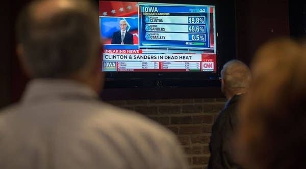 People look on as a television broadcast declares Senator Bernie Sanders and Hillary Clinton in a dead heat for delegates at the conclusion of the Iowa caucuses at the Boogaloo Cafe on February 1, 2016 in Burlington, Iowa.