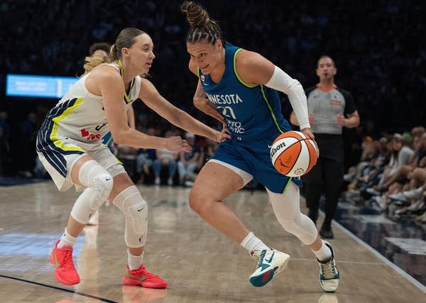 A Lynx basketball player dribbles the ball near the edge of the court while facing off against an opposing player.