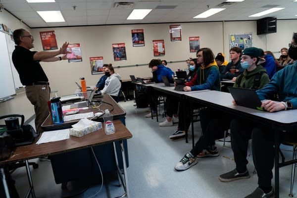 Students listen as a teacher speaks to them in class.