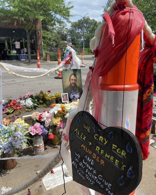 A heart-shaped ornament hangs off a traffic cone in front of flowers and a portrait of Alex Pretti