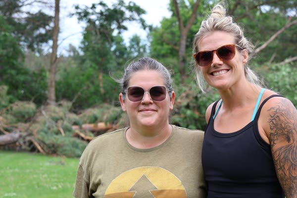 Two women pose for a photo with a downed tree in the background.