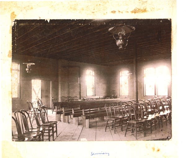 An archival image of rows of chairs and pews in a 19th century classroom.
