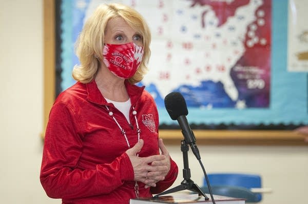 A woman in a face mask talks in front of a microphone.