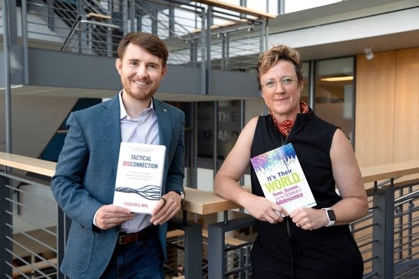 two people smiling for a portrait while holding books