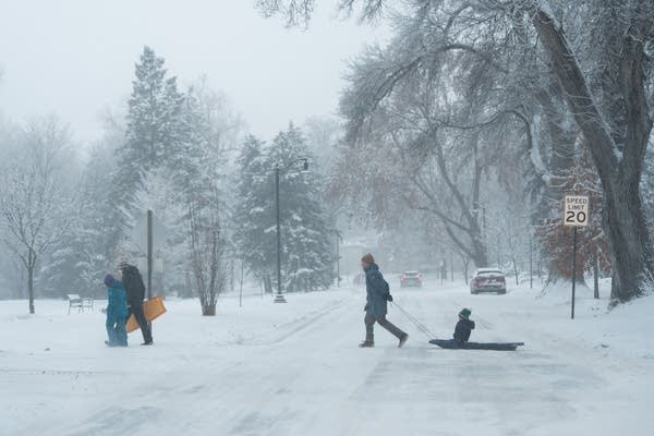 A man pulls a child on a sled across the street