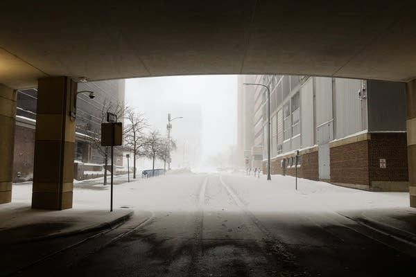 A snowy downtown street is seen from under a bridge.