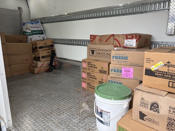 A bucket and stacks of cardboard boxes sit in a truck's cargo area.