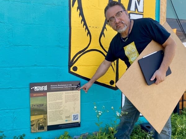 A man points to a sign near a mural.