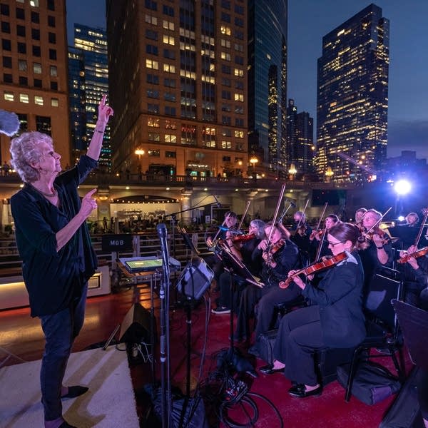 Poster An orchestra performing on the deck of a boat cruising in a river through a city 