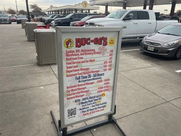 Outside near a parking lot, a sign listing starting wages for different positions at Buc-ee's