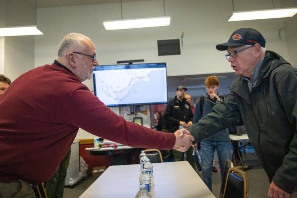 Two men shake hands over a table