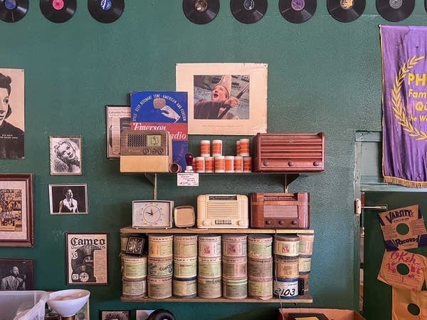 Vintage radios are displayed on a shelf up against a dark green wall.