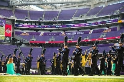 A marching band performs on the field of a football stadium.