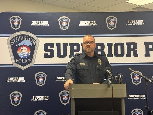 A police officer speaks from a podium in front of a banner with the Superior Police logo.