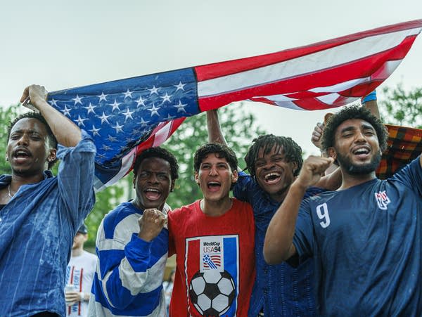 Fans shelter beneath an American flag during a FIFA World Cup watch party organized by Minnesota United FC between Brit’s Pub and the Minnesota Orchestra on Friday, June 12, 2026, in Minneapolis, Minn. Heavy rain fell throughout much of the match, but supporters remained gathered outdoors as the United States opened its first home World Cup in 32 years with a 4-1 victory over Paraguay in Inglewood, Calif. Folarin Balogun scored twice as the Americans built a 3-0 halftime lead, matching the largest World Cup victory in team history and setting a U.S. record with four goals in a World Cup match.
