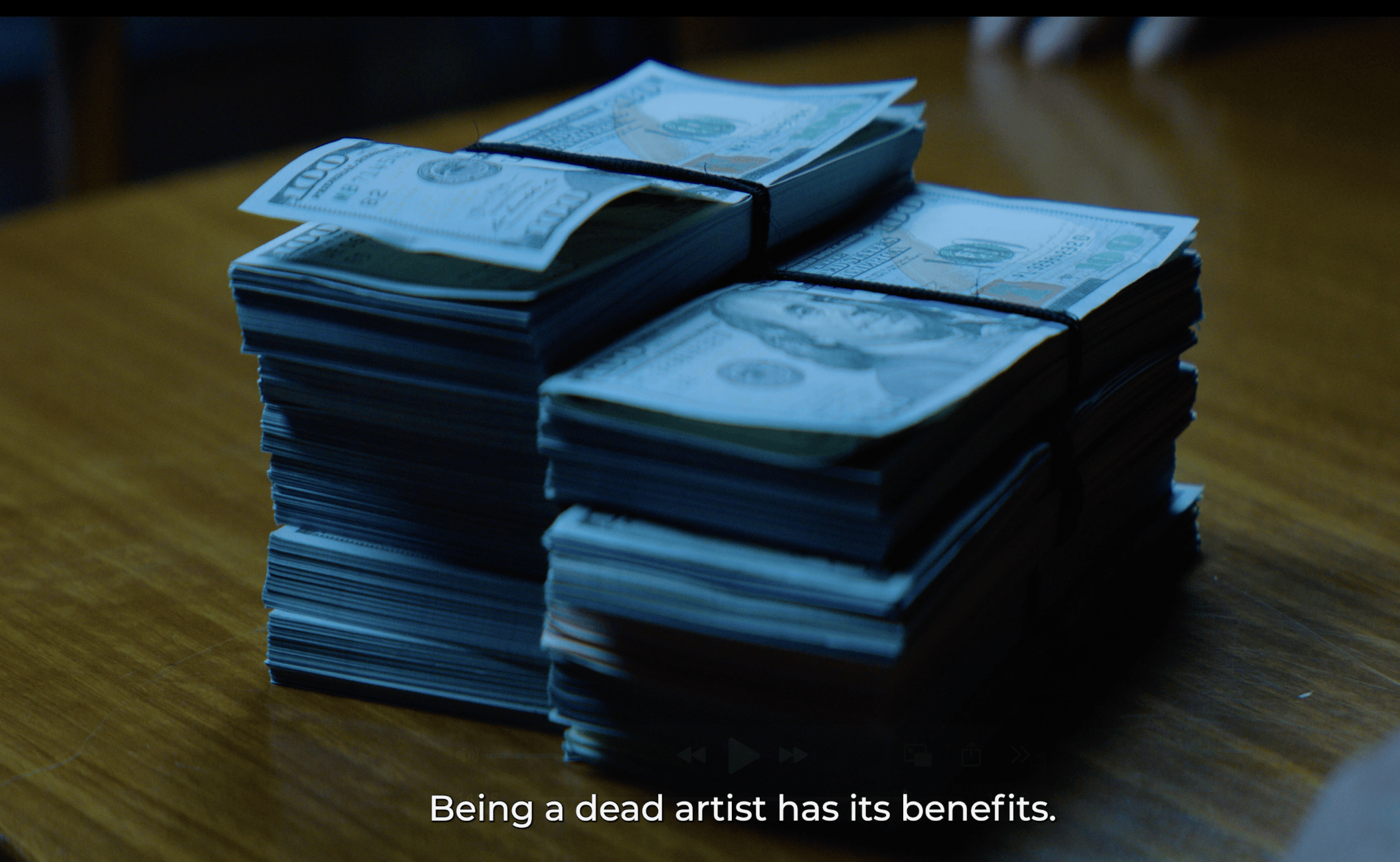 Still from a film of two stacks of $100 bills on a wooden table.