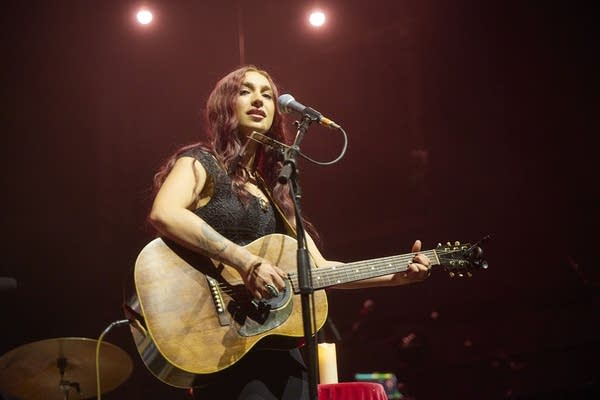 A woman sings and plays guitar onstage in a large music venue