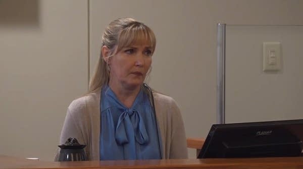 A woman sits at the witness stand in a courtroom.