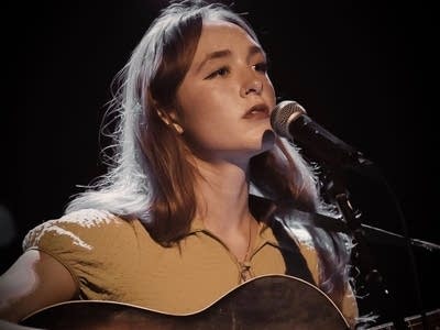 A woman sings and plays guitar onstage 