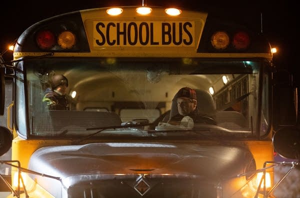 A man sits in the driver seat of a bus at night. 