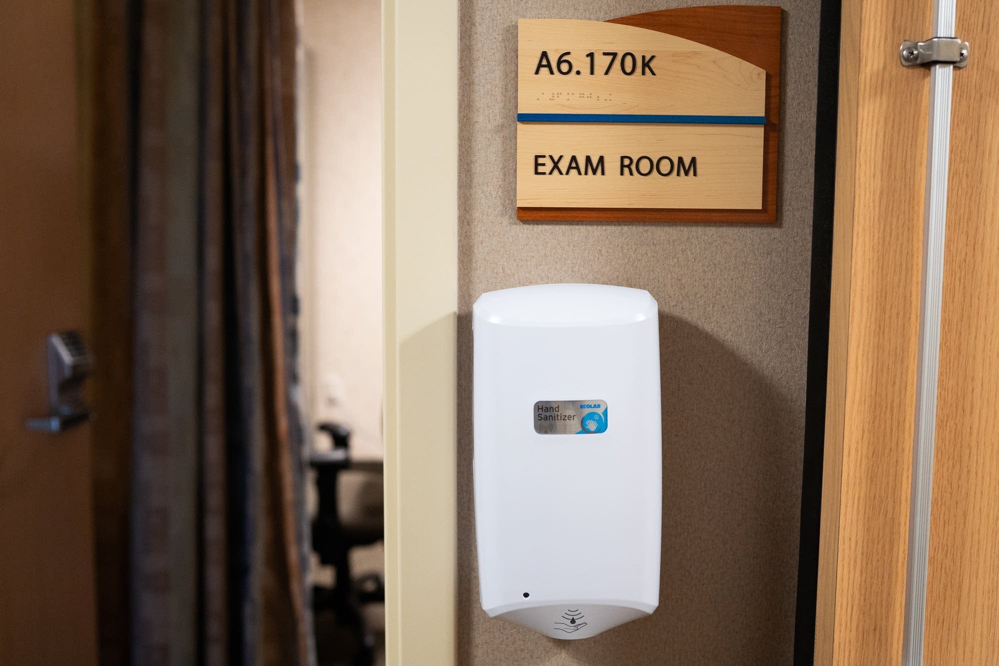 An automated hand sanitizer station hangs outside of an exam room