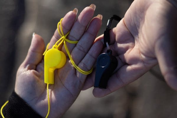 Two hands are holding whistles