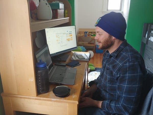 A man sitting in front of a computer at a desk in a child's bedroom.