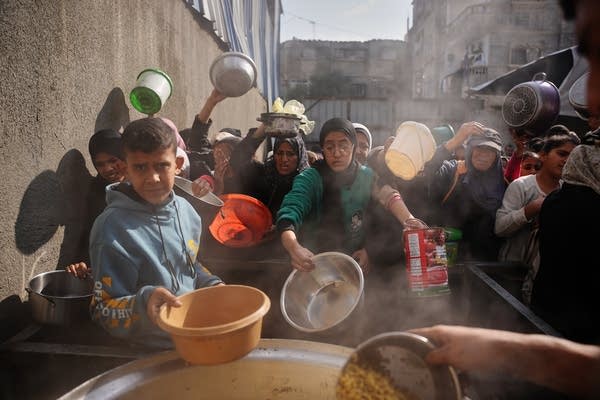 People hold bowls out to receive food donations.