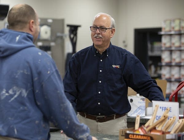 Two men talk at a counter. 