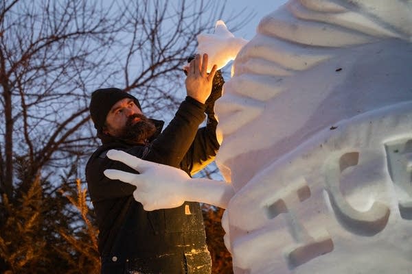 A man adds a small piece to a larger snow sculpture.