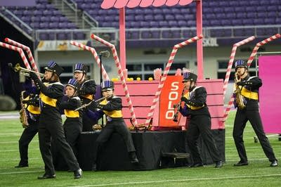 A marching band performs on the field of a football stadium.