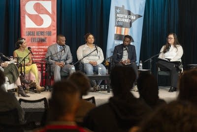 Five people sit on a stage in front of an audience.