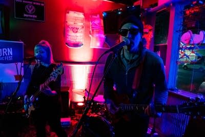 Two musicians sing and play instruments in a bar