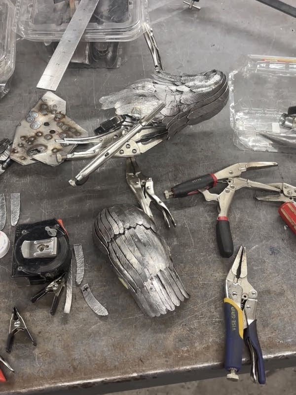 The pieces of steel that are being fashioned into a raven. There are clips and pliers scattered on the workstation.