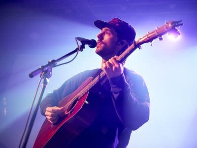 A man plays an acoustic guitar and sings into a microphone.