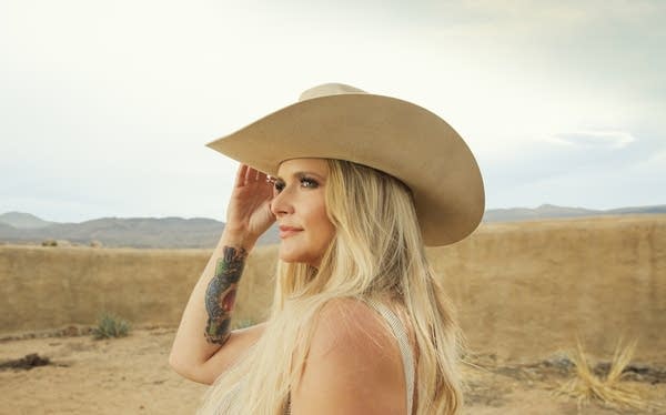 A woman in a cowboy hat stands outdoors on a vast, arid plain