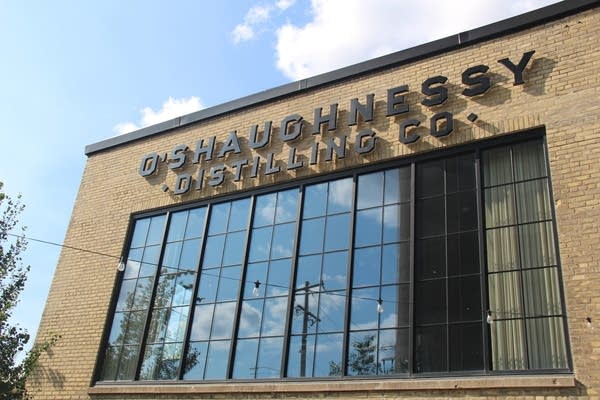 Exterior shot of a distillery. It's a light brick building with a large pane of windows.