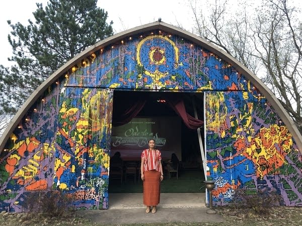 A person stands in front of the entrance of a barn that is vibrantly painted.