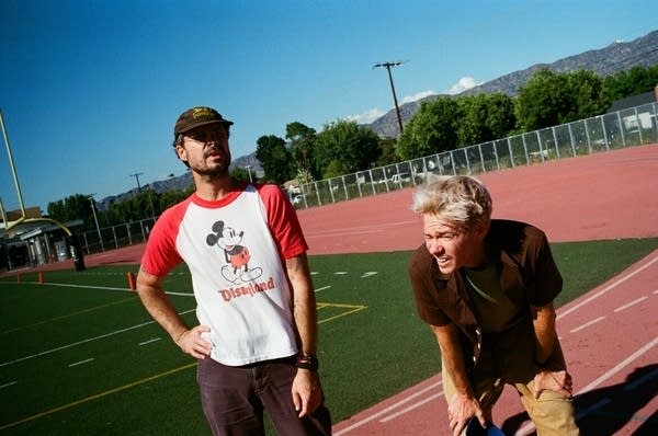 Two guys stand on a track; one of them looks a bit winded, with hands on his knees