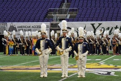 A marching band performs on the field of a football stadium.