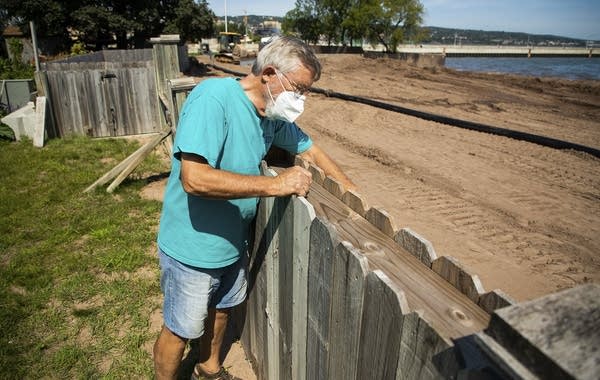 A person leans over a fence that separates his yard and beach. 