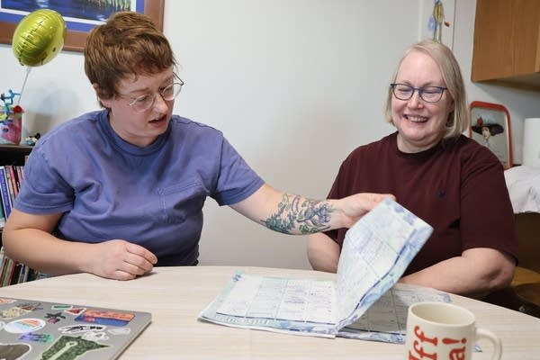 Two women sit at a kitchen table as they both look at a paper calendar.