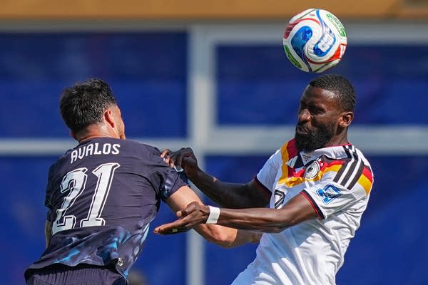 A soccer player from Germany hits a header as he battles for the ball with a Paraguay player.